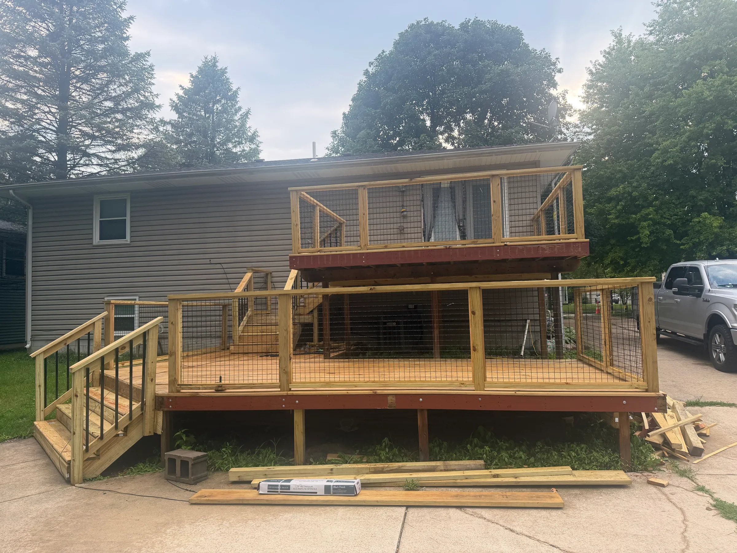 Exterior view of new deck construction showing structural framing with pressure-treated posts and beams properly secured, white railing system, and completed decking installation on residential home addition.